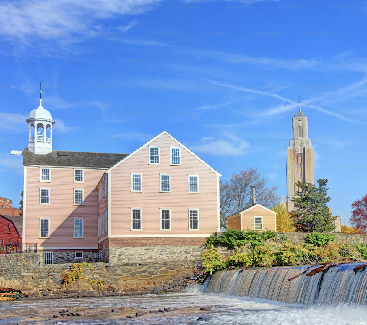 Historic buildings beside a broad waterfall under a bright blue sky.