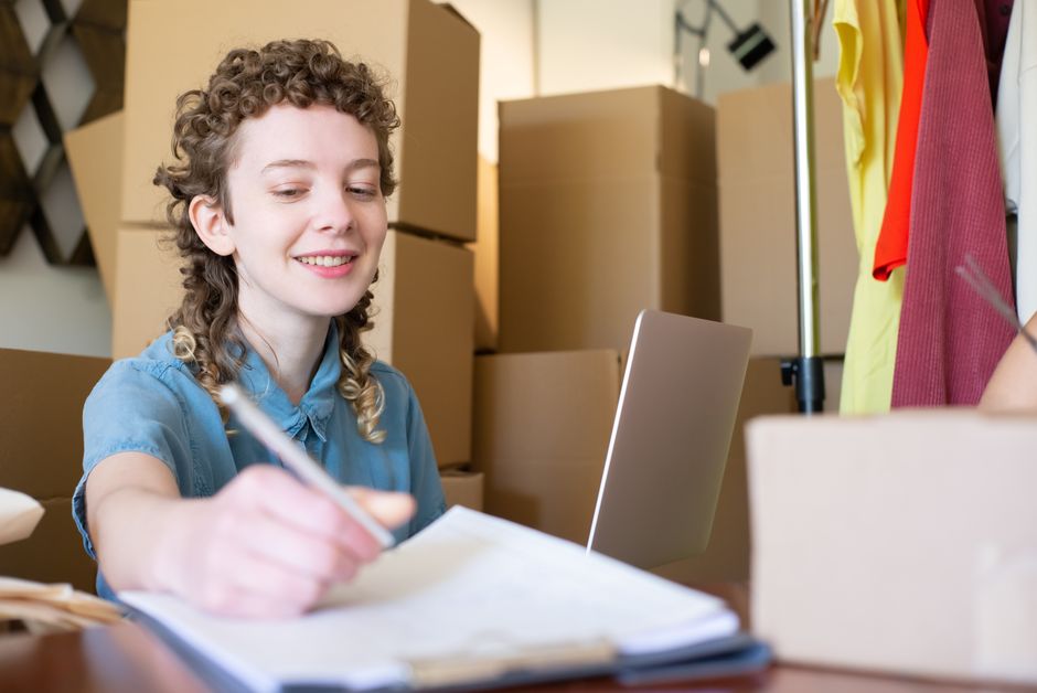A small-business owner works on a laptop beside packages.