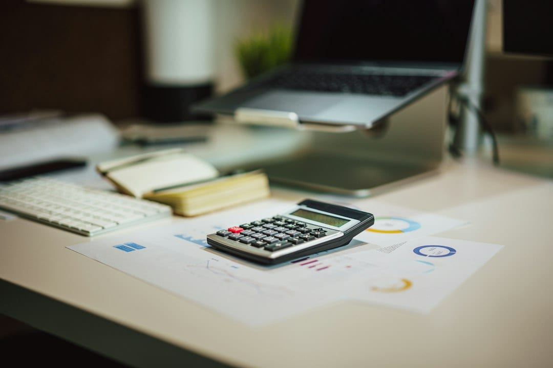 A calculator sits beside a laptop on a work surface.