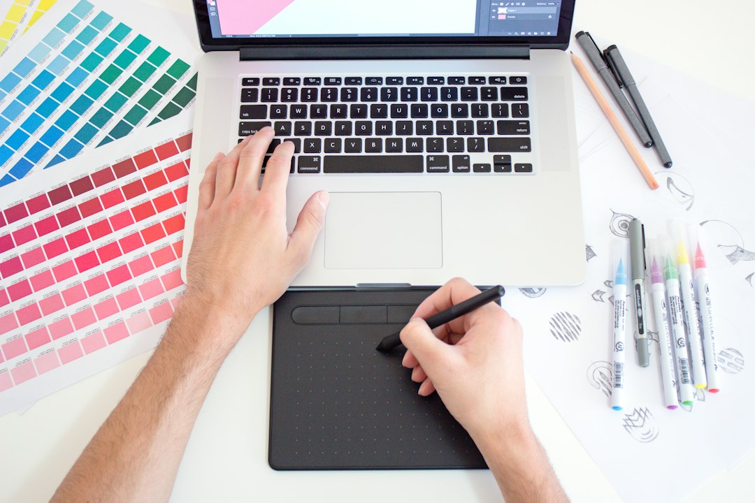 A designer works with a drawing tablet, laptop, and color swatches.