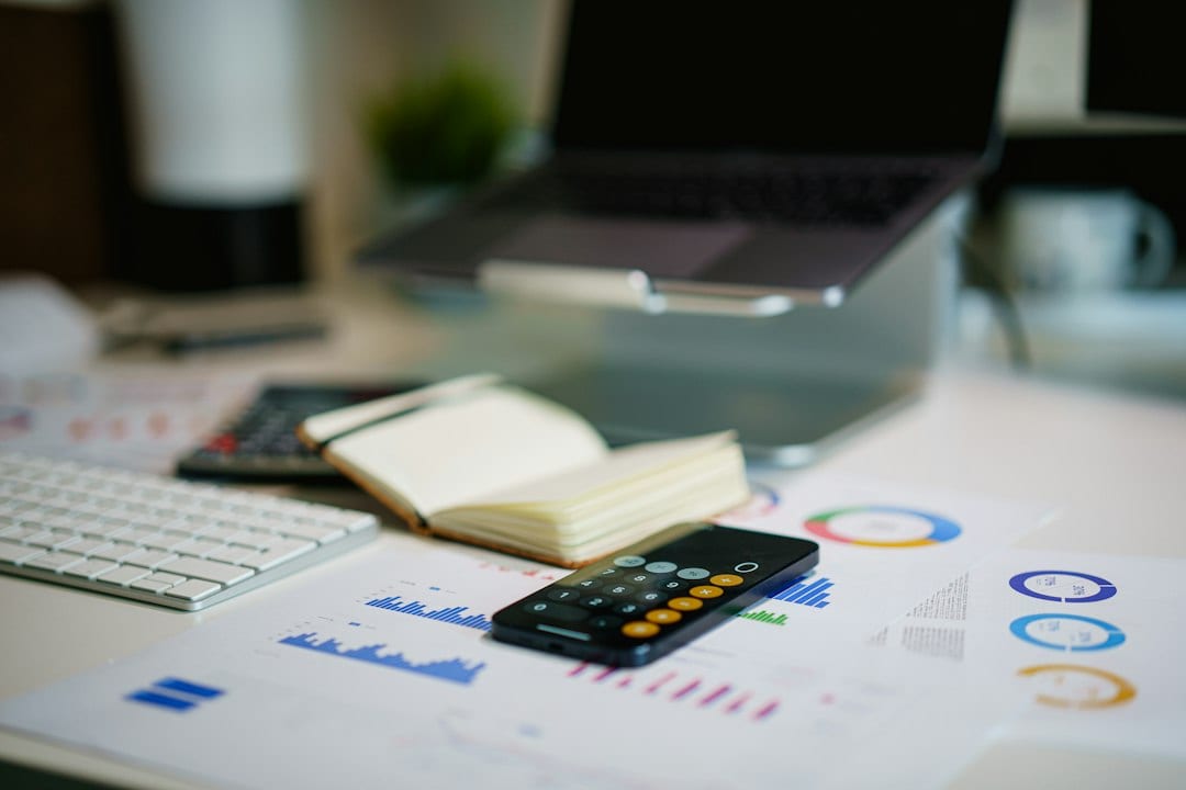 A smartphone and financial charts sit on an office desk.