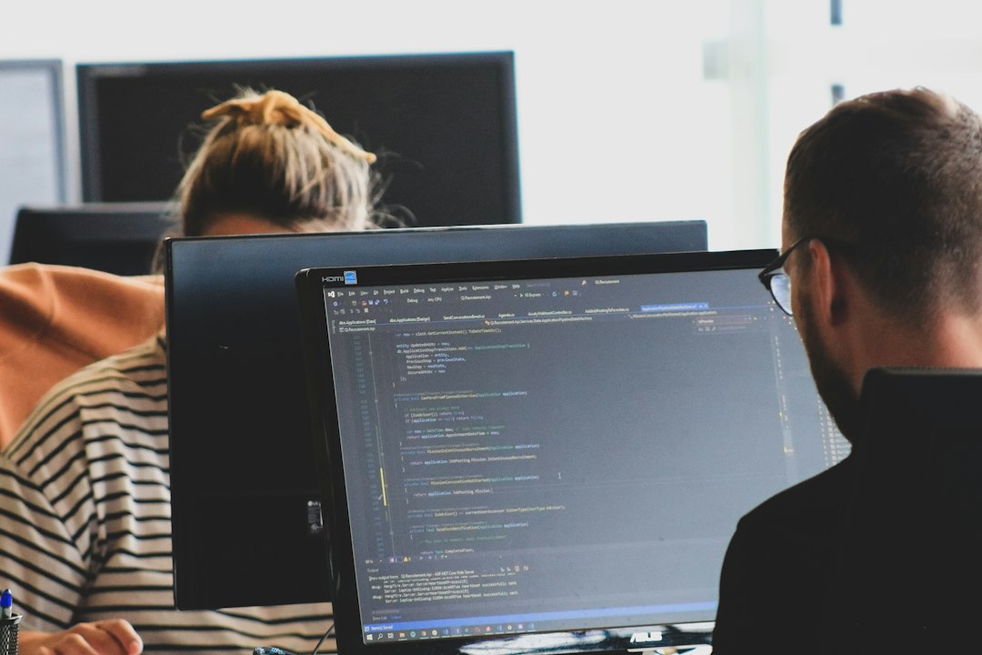 Two people work on code at desktop monitors.