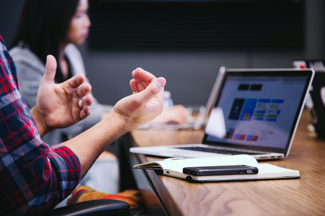 A person gestures while colleagues meet around a laptop.